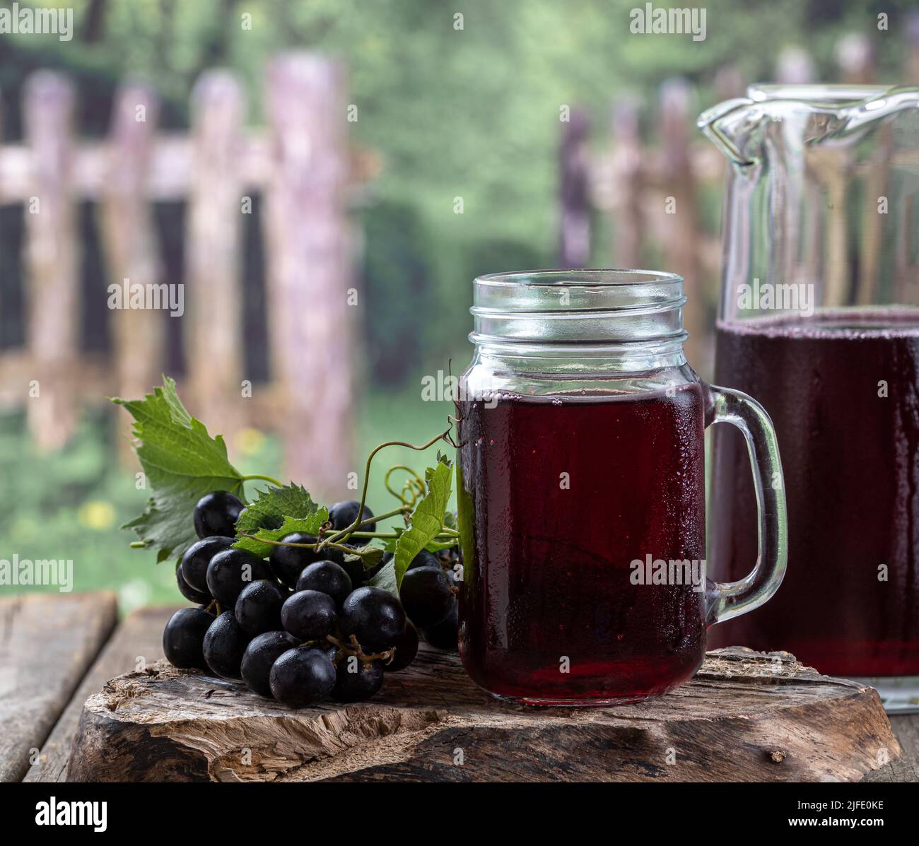 Bicchiere e caraffa di succo d'uva con uve fresche su blocco di legno con sfondo rurale Foto Stock