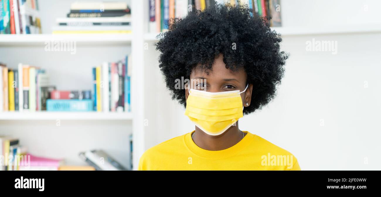 Donna afroamericana con maschera gialla come protezione contro il virus Covid-19 Foto Stock