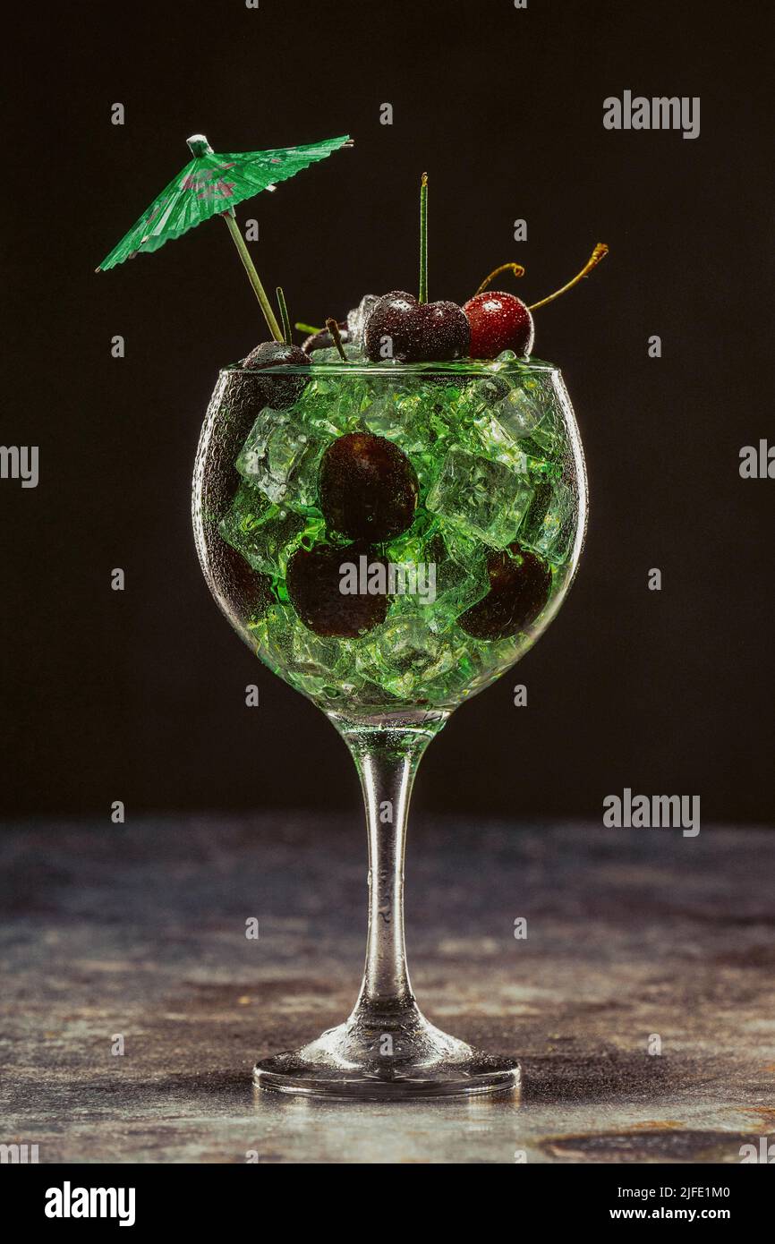 Cocktail verde con ghiaccio e ciliegie in un bicchiere decorato con ombrelloni. Foto Stock