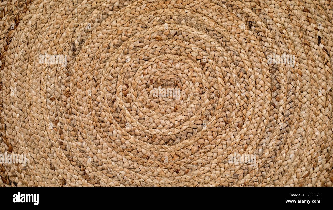 Tappeto in rafia naturale rotondo con un disegno intrecciato a spirale e cerchi concentrici che creano una texture ideale per sfondi e risorse grafiche. Foto Stock
