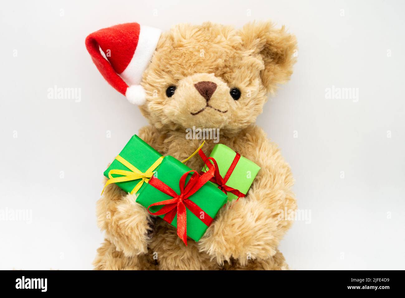 Un orsacchiotto peluche giocattolo in un cappello rosso di Babbo Natale con un pompom su un orecchio, tenendo le scatole regalo verdi nelle sue zampe. Sfondo bianco, spazio di copia. Il co Foto Stock