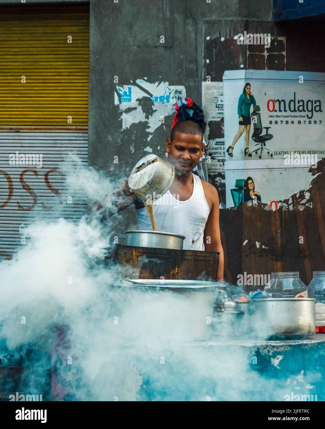 Kolkata, India - 26 Giugno, 2022: Un venditore di tè sulla strada che fa il tè al mattino presto con fumo in primo piano. Messa a fuoco selettiva. Foto Stock