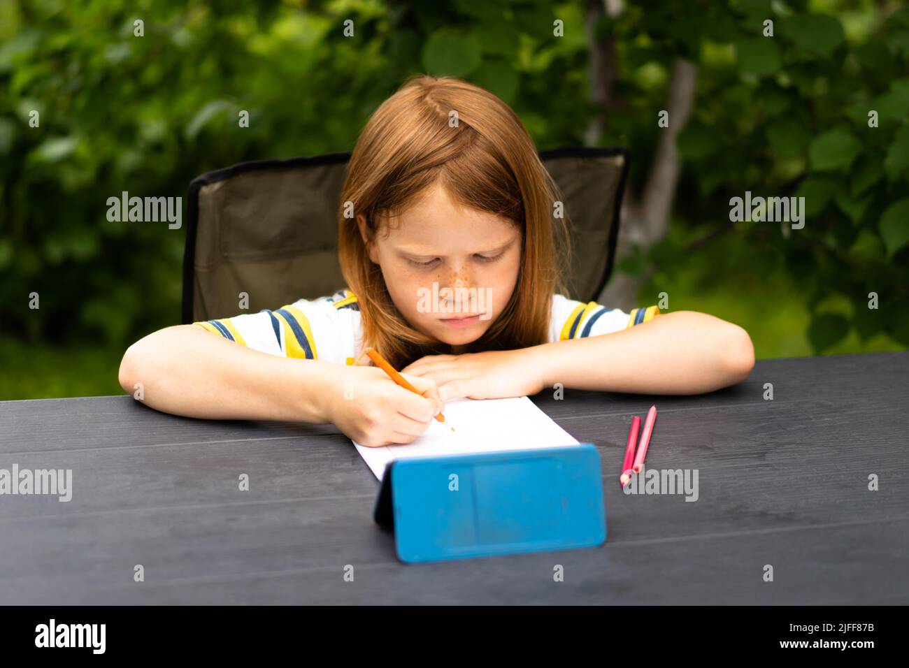 Apprendimento remoto online. I ragazzi della scuola con il telefono hanno una chat in videoconferenza con l'insegnante e il gruppo di classe. Il bambino impara nel giardino . Foto Stock