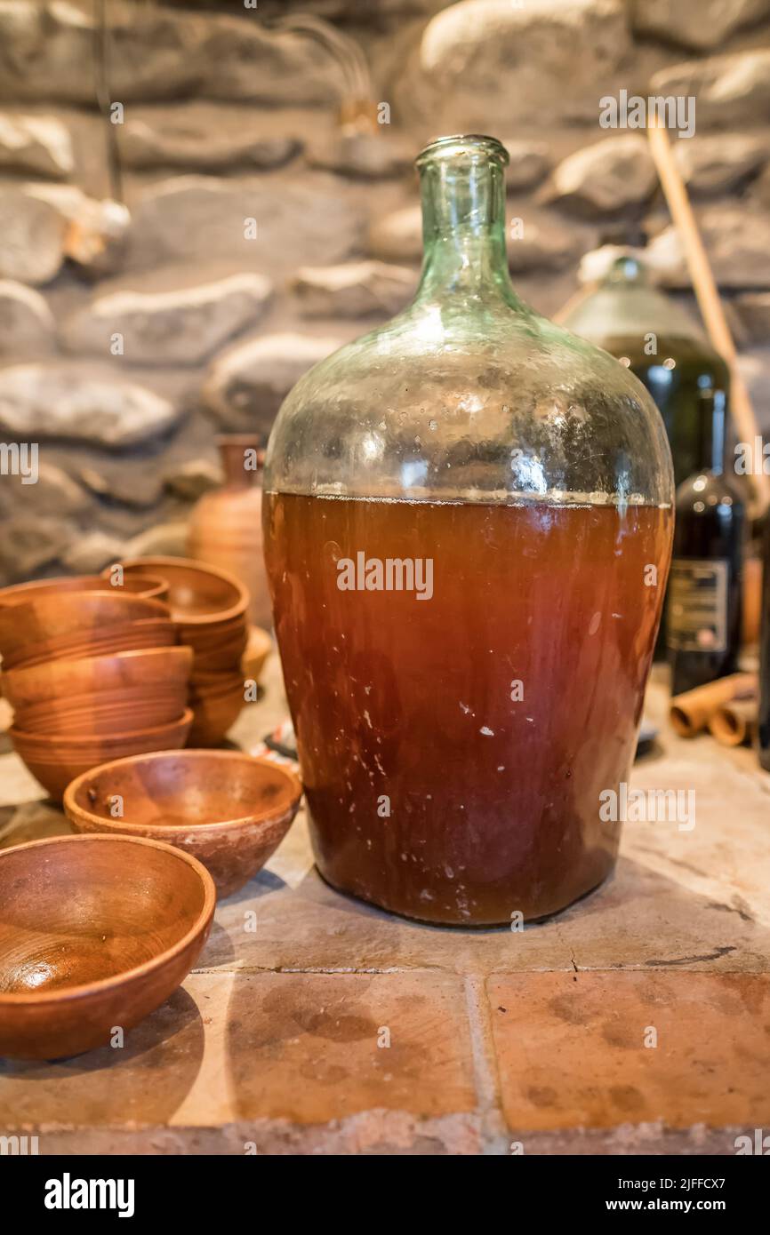 Vino giovane in grande bottiglia di vetro accanto alla brocca in terracotta georgiana d'epoca in un'autentica cantina georgiana. Foto Stock