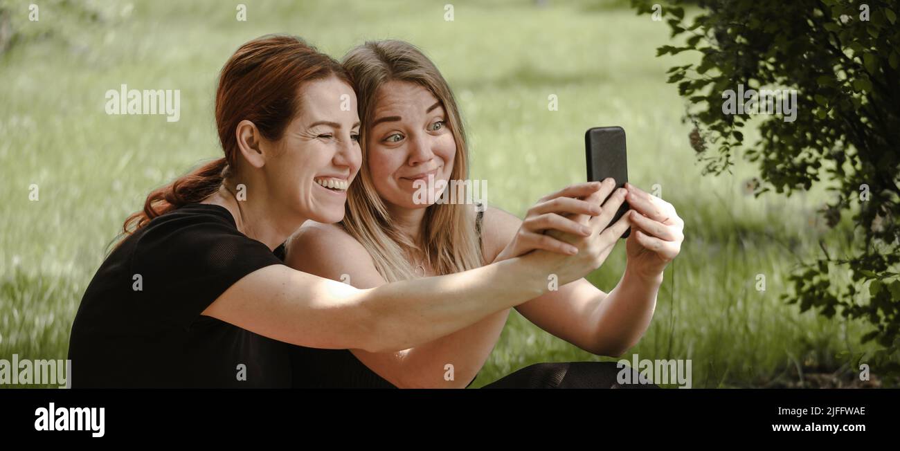 Due donne che si divertono al picnic. Amici su coperta comunicando felicemente facendo selfie. Allegra femmina parlare all'aperto, la gente ridendo e avendo Foto Stock