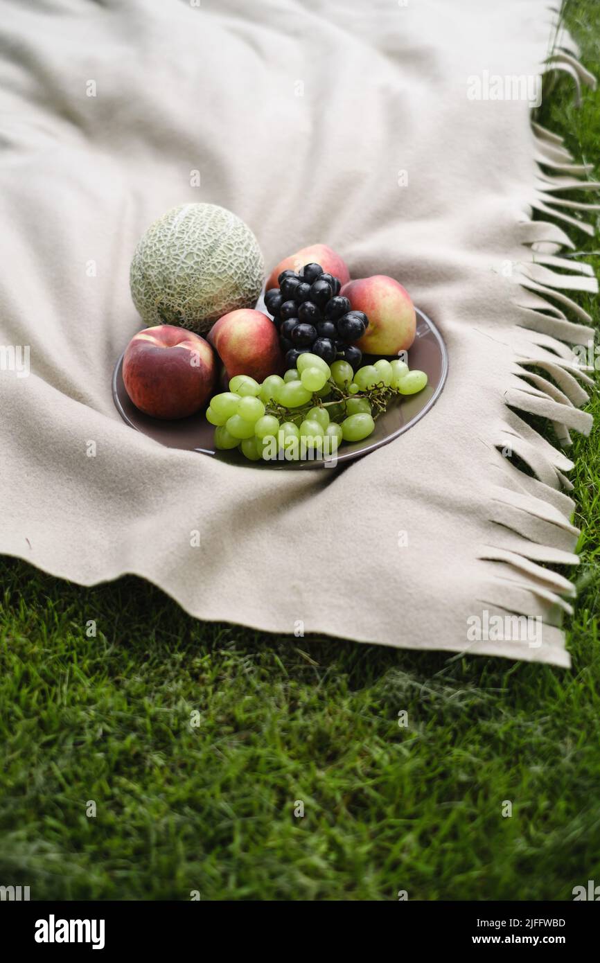 Frutta fresca sul piatto sulla coperta all'aperto nel parco. Uva estiva, pesca, melone. Picnic con cibo colorato sull'erba. Spazio di copia. Foto Stock