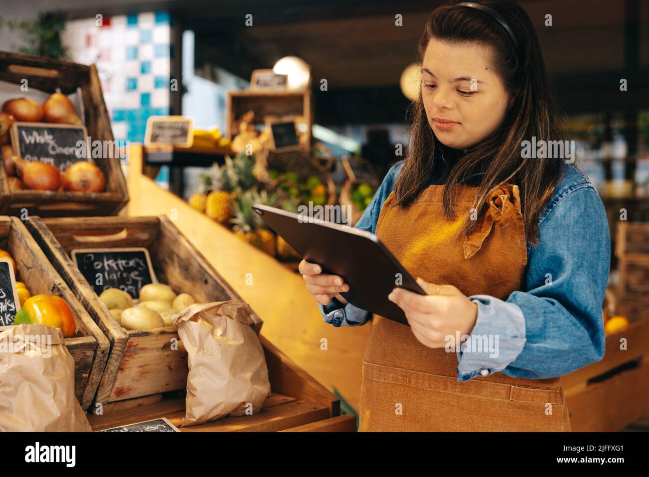 Conservatore con sindrome di Down utilizzando un tablet digitale nella sezione di prodotti freschi di un negozio di alimentari. Donna con una disabilità intellettuale lavoro io Foto Stock