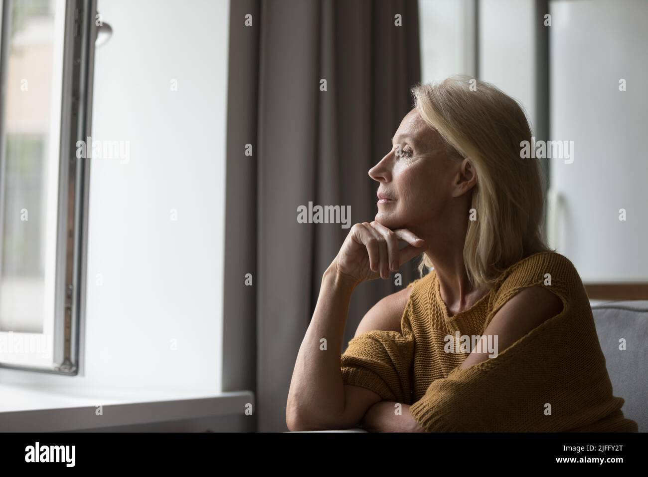 Donna anziano e pensiva che riposa sul divano che guarda fuori dalla finestra Foto Stock