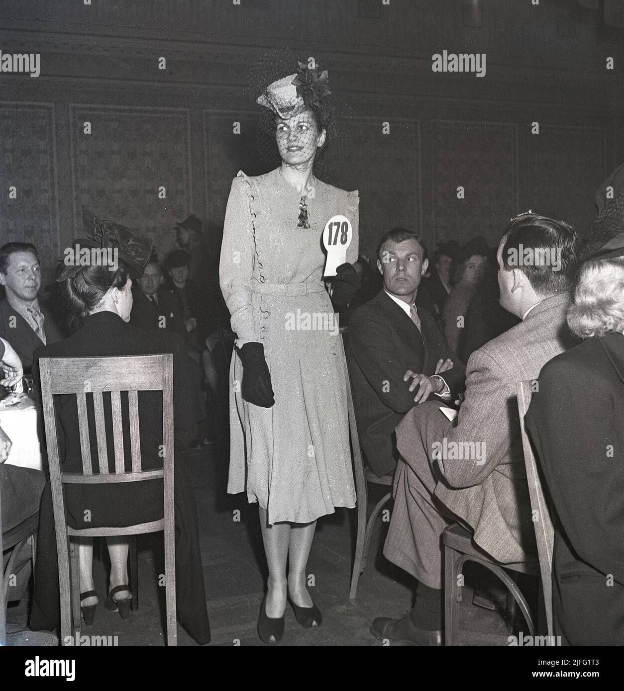 Moda femminile nel 1940s. Una giovane donna in un abito del 1946. Un abito con la giusta lunghezza, cappello e guanti coordinati. La sfilata di moda femminile di quest'anno continua davanti alle persone di un pubblico. Svezia 1946 Kristoffersson T148-6 Foto Stock