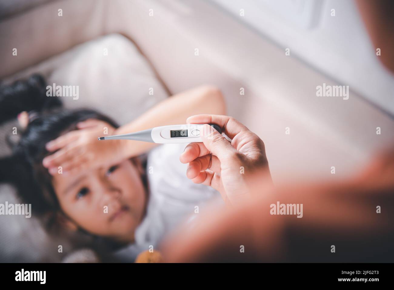 Ragazzo malato. Madre genitore controllo della temperatura della sua figlia ammalata con termometro digitale in bocca, bambino che si stendeva a letto prendendo la misura della sua tempera Foto Stock