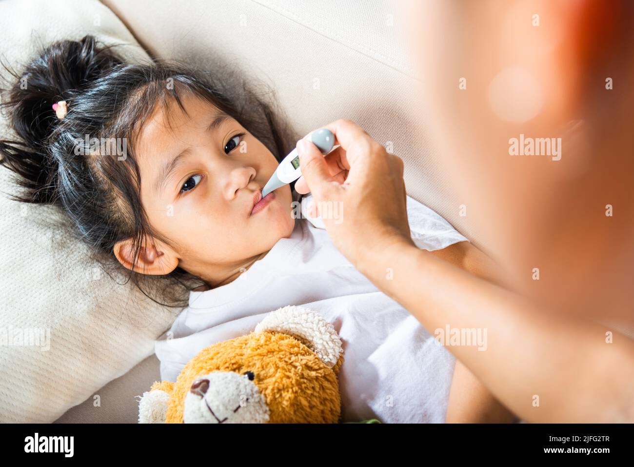 Ragazzo malato. Madre genitore controllo della temperatura della sua figlia ammalata con termometro digitale in bocca, bambino che si stendeva a letto prendendo la misura della sua tempera Foto Stock