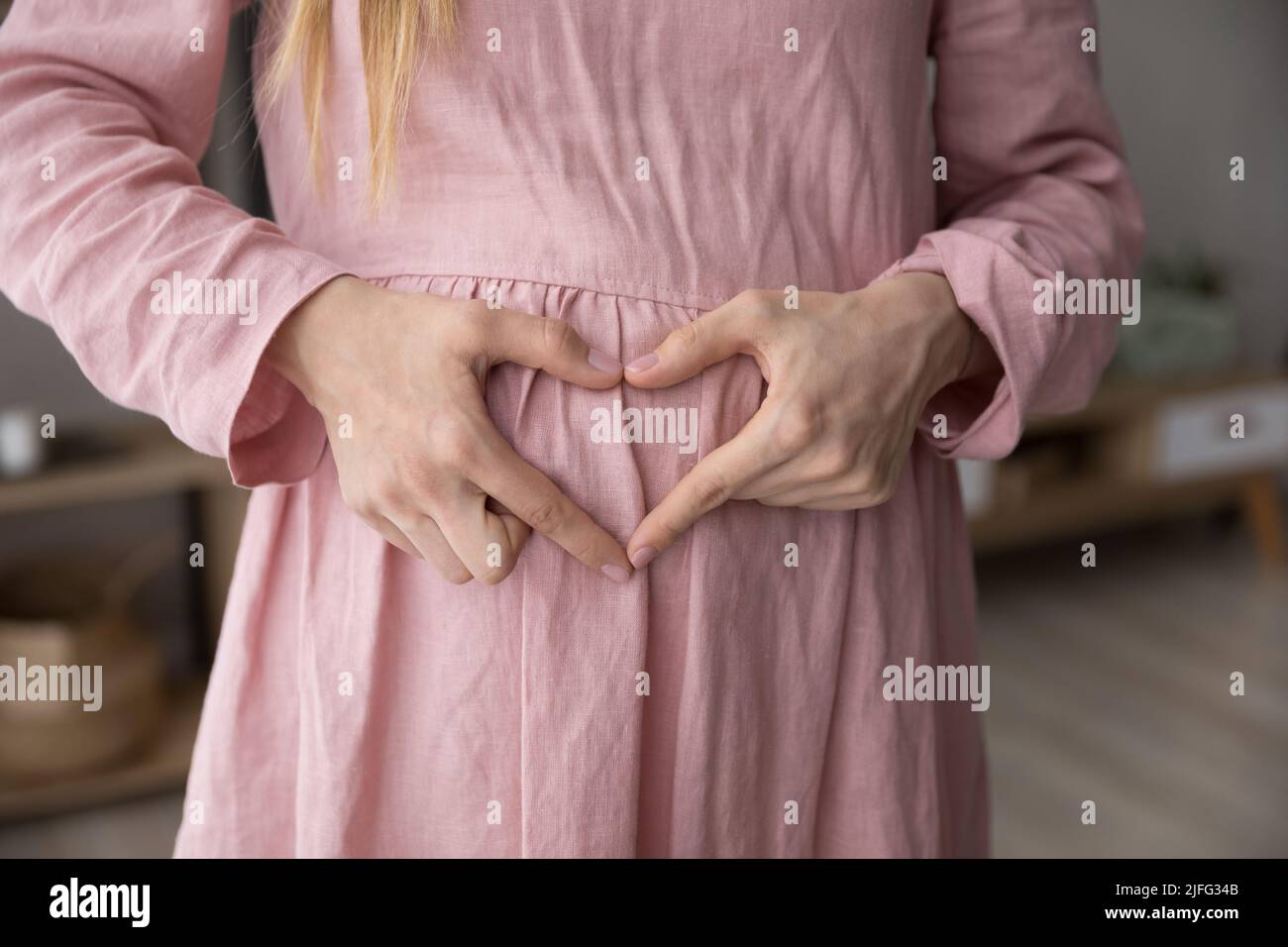 La donna incinta forma il cuore con le dita sul ventre, primo piano Foto Stock