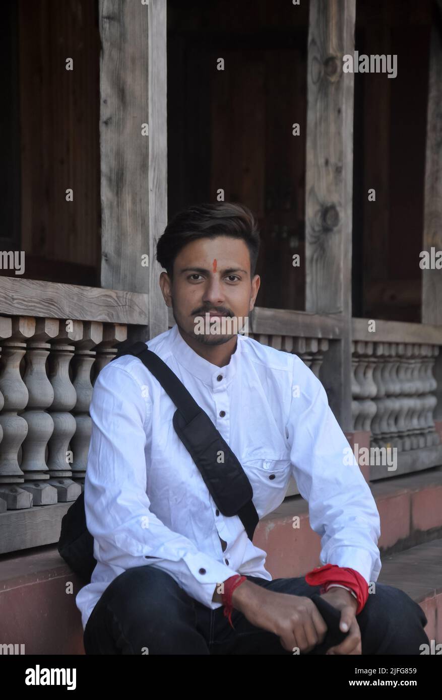 Un giovane indiano che guarda bene la macchina fotografica mentre si siede sulle scale del tempio Foto Stock