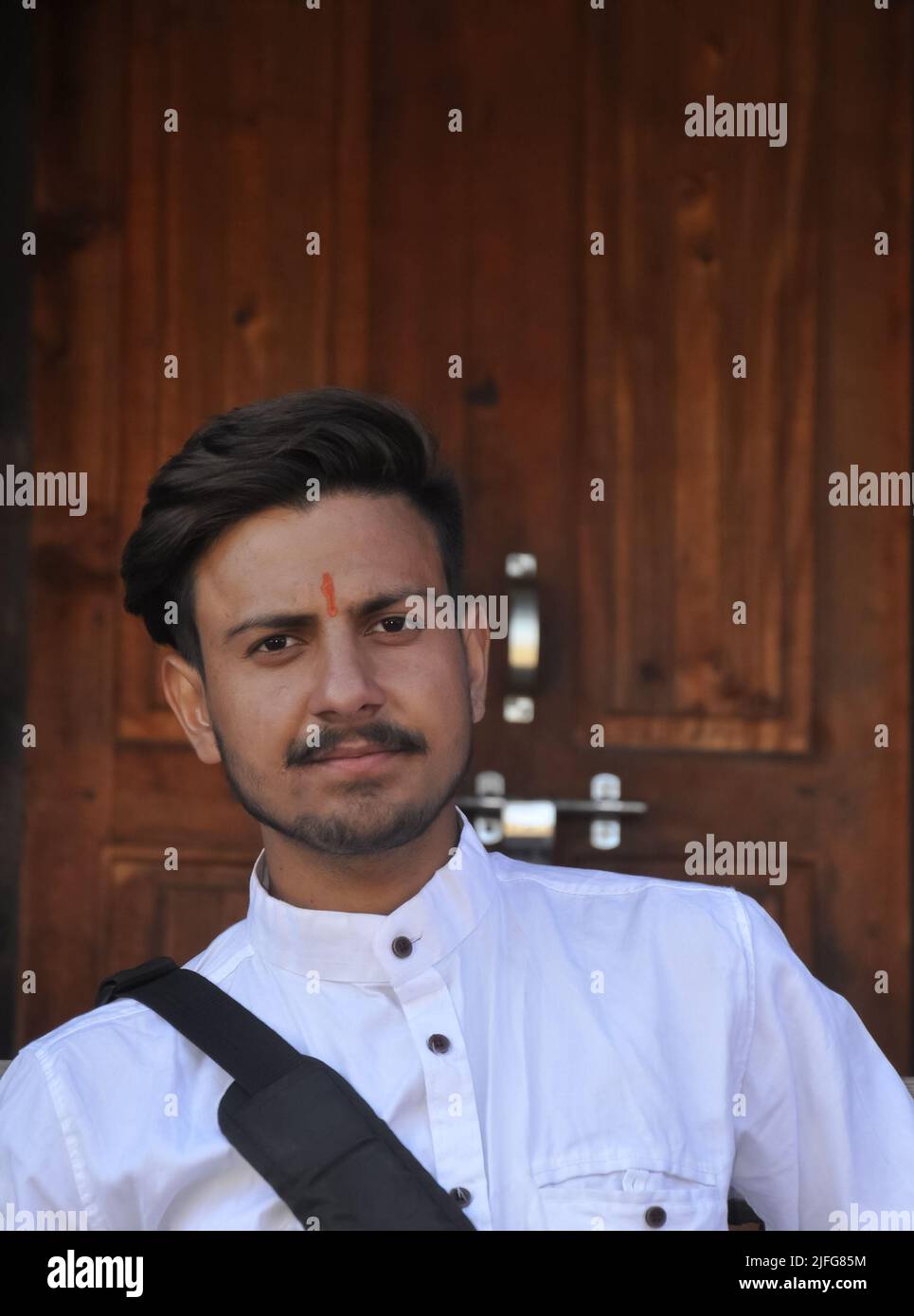 Primo piano di un bel ragazzo indiano giovane guardando la macchina fotografica con seduta contro porta di legno Foto Stock
