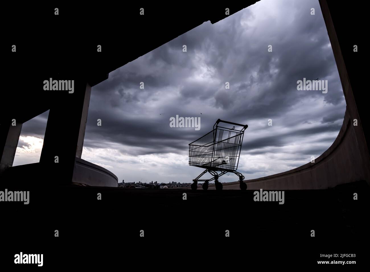 Un carrello per lo shopping su un parcheggio sul tetto di un centro commerciale abbandonato durante l'epidemia di Coronavirus, nubi di pioggia scuro sullo sfondo. Foto Stock