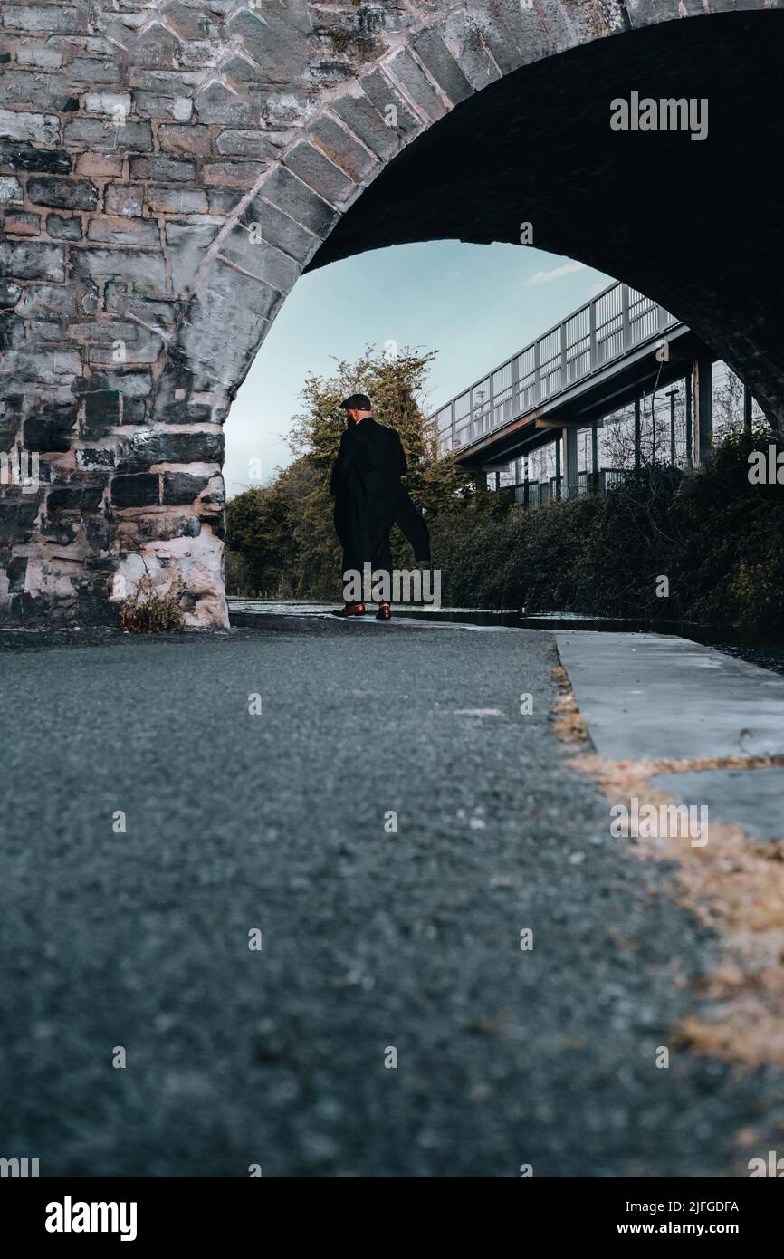 Elegante gangster uomo a piedi, passando tunnel sotto un ponte ferroviario 1920s tema. Uomo alla moda brutale sicuro. Foto Stock