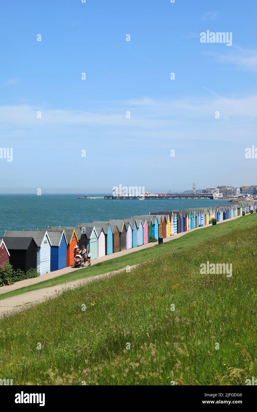 Colorate capanne sulla spiaggia a Herne Bay, con il molo in lontananza, nel nord Kent, Regno Unito Foto Stock