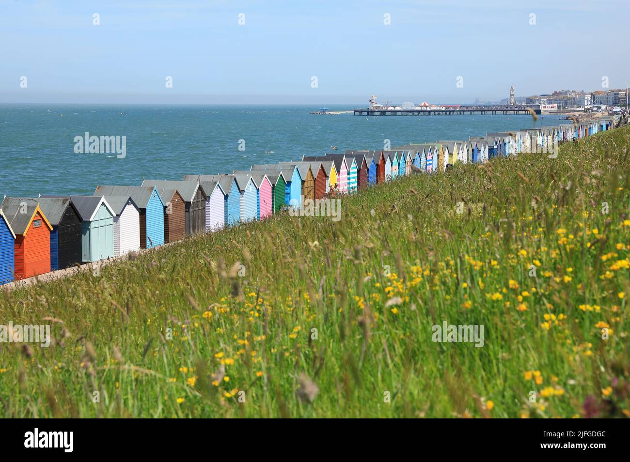 Colorate capanne sulla spiaggia a Herne Bay, con il molo in lontananza, nel nord Kent, Regno Unito Foto Stock