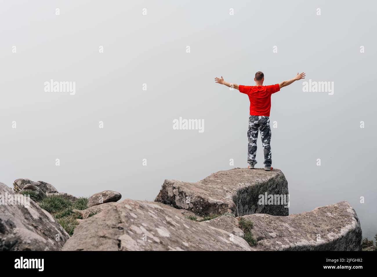 L'escursionista in cima alla montagna gode della vista aerea, sollevando le mani sopra le nuvole. Monte Pidan. Foto di alta qualità Foto Stock