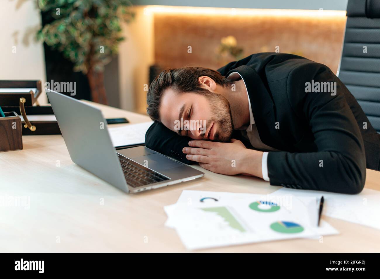 Esausto uomo d'affari caucasico stanco, ceo, responsabile aziendale, in un vestito formale, dormire sul posto di lavoro dopo una dura giornata di lavoro, l'impiegato d'ufficio ha bisogno di riposo, soffre di stanchezza cronica e mancanza di sonno Foto Stock