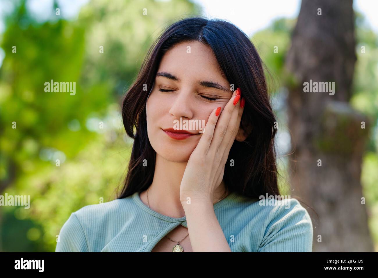 Giovane donna bruna con tee turchese e corteccia arancione sul parco della città, all'aperto toccando la bocca con mano con espressione dolorosa a causa di dentifricio Foto Stock