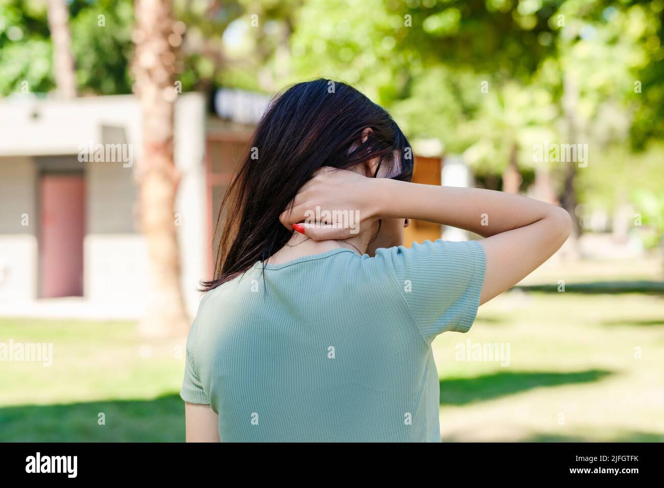 Giovane bella donna con tee turchese sul parco cittadino, all'aperto sensazione di dolore alle spalle articolare dolore alla schiena, concetto di fibromialgia, close up posteriore vie Foto Stock