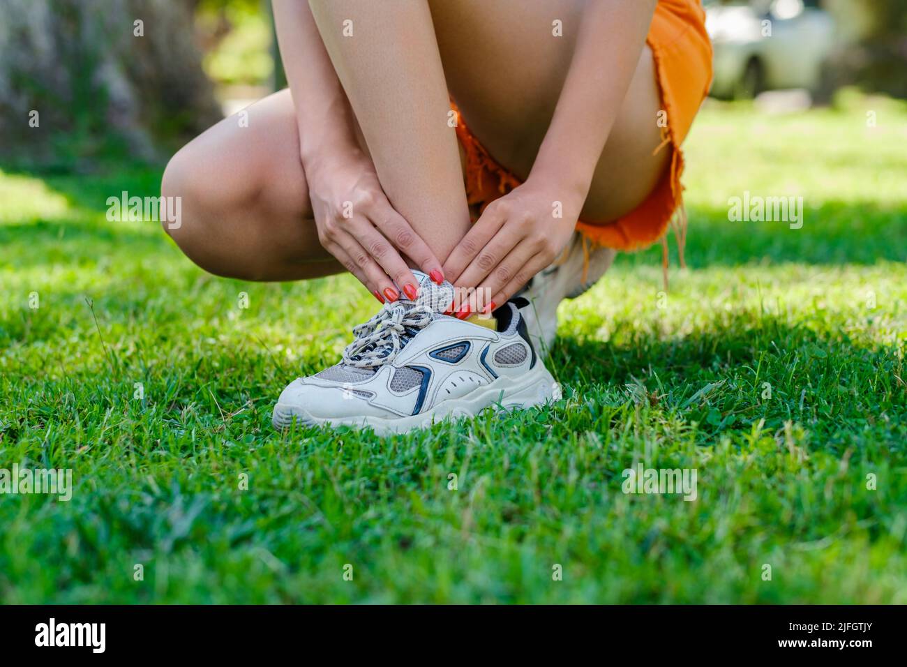 Cute donna millenaria che indossa la tee in piedi sul parco cittadino, all'aperto che soffre di una lesione alla caviglia durante l'esercizio e la corsa. Assistenza sanitaria e sport co Foto Stock