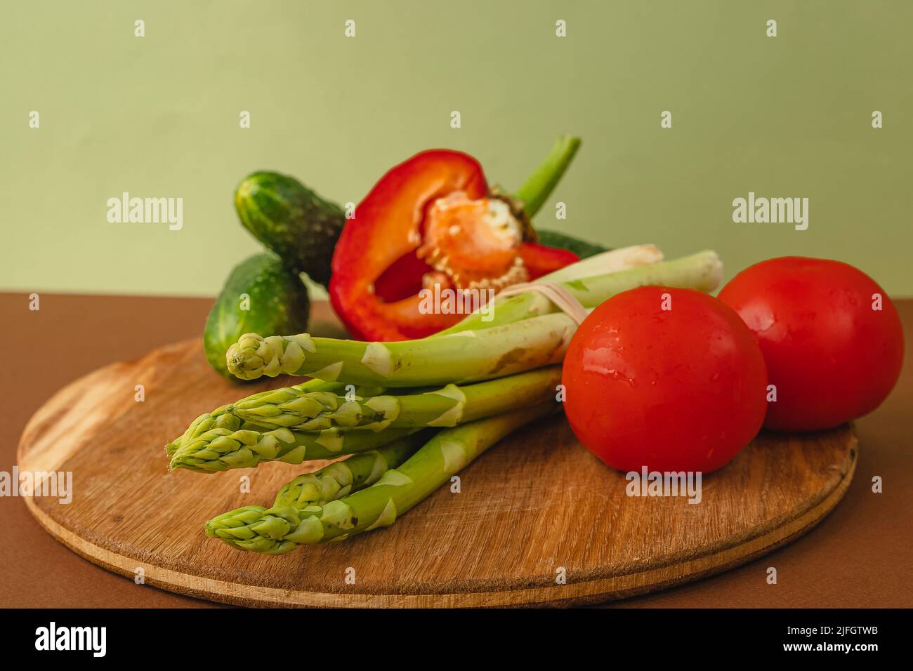 Le verdure si trovano su un asse di legno: Pomodori, asparagi, cetrioli, peperoni rossi. Marrone, sfondo verde chiaro. Luogo per il testo Foto Stock