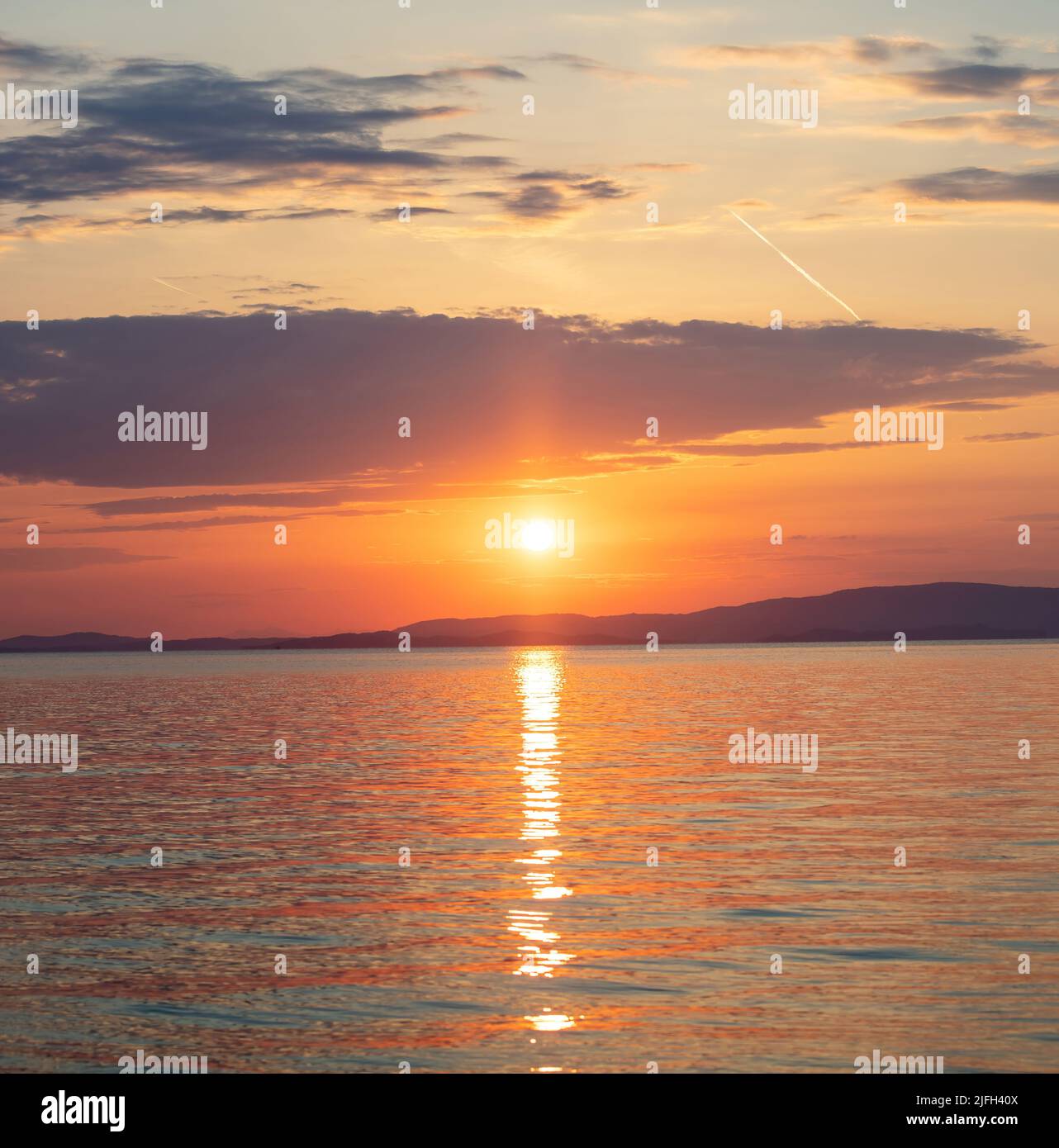 Tramonto sul Mar Egeo. Grecia. Sole che cade dietro terra scura, riflessi dorati su ondulato acqua dell'oceano. Cielo e nuvole di colore arancione Foto Stock