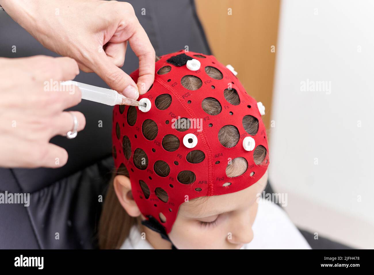 Medico che applica un liquido al copricapo di un paziente per la terapia del biofeedback Foto Stock