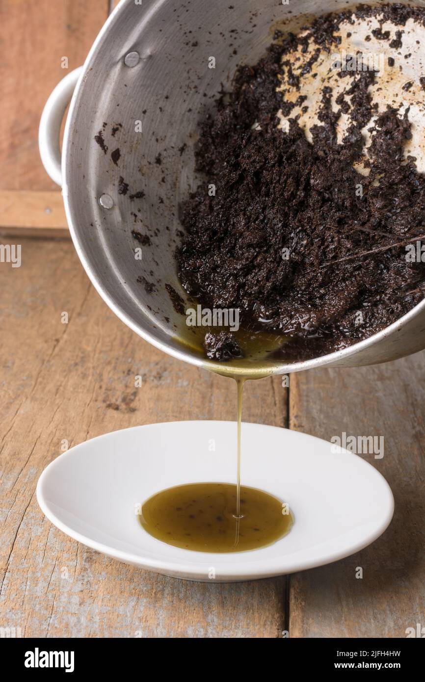 olio di erbe ayurvediche fatto in casa che versa in un piatto bianco, henné, aloe vera e polvere di tè mescolati e bolliti con olio di cocco Foto Stock