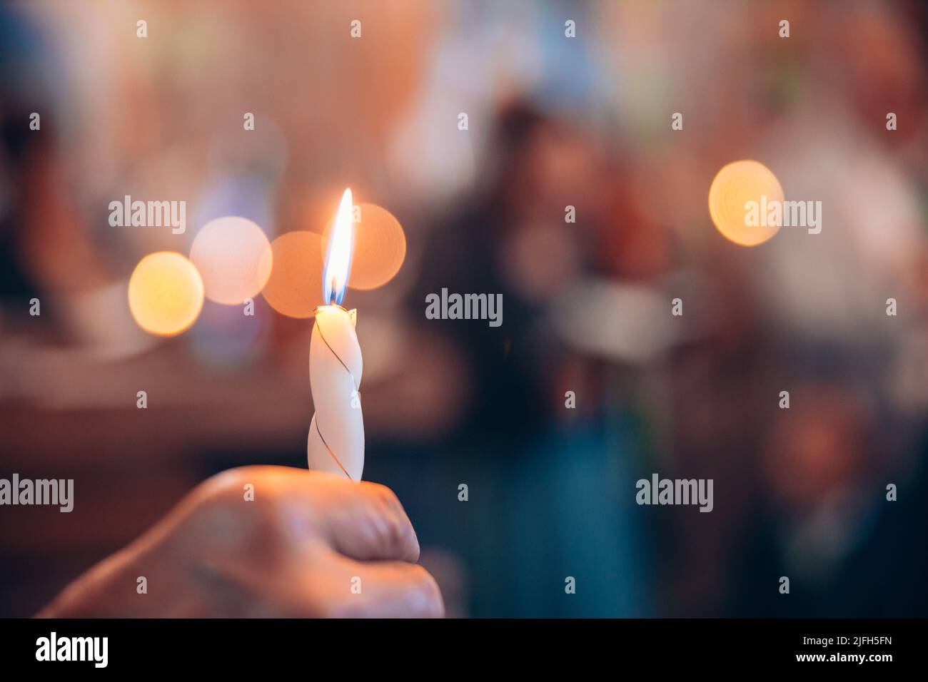 Donna che tiene una candela in fiamme in una chiesa per una cerimonia. Bokeh candela luci sullo sfondo. Religione del cristianesimo. Foto di alta qualità Foto Stock