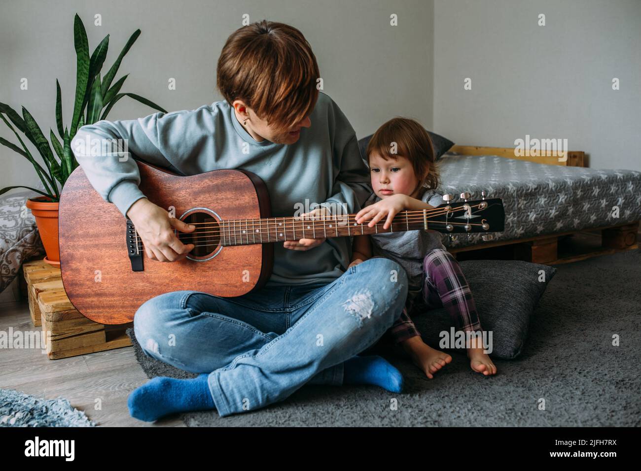 La bambina suona la chitarra con la madre sul pavimento a casa Foto Stock