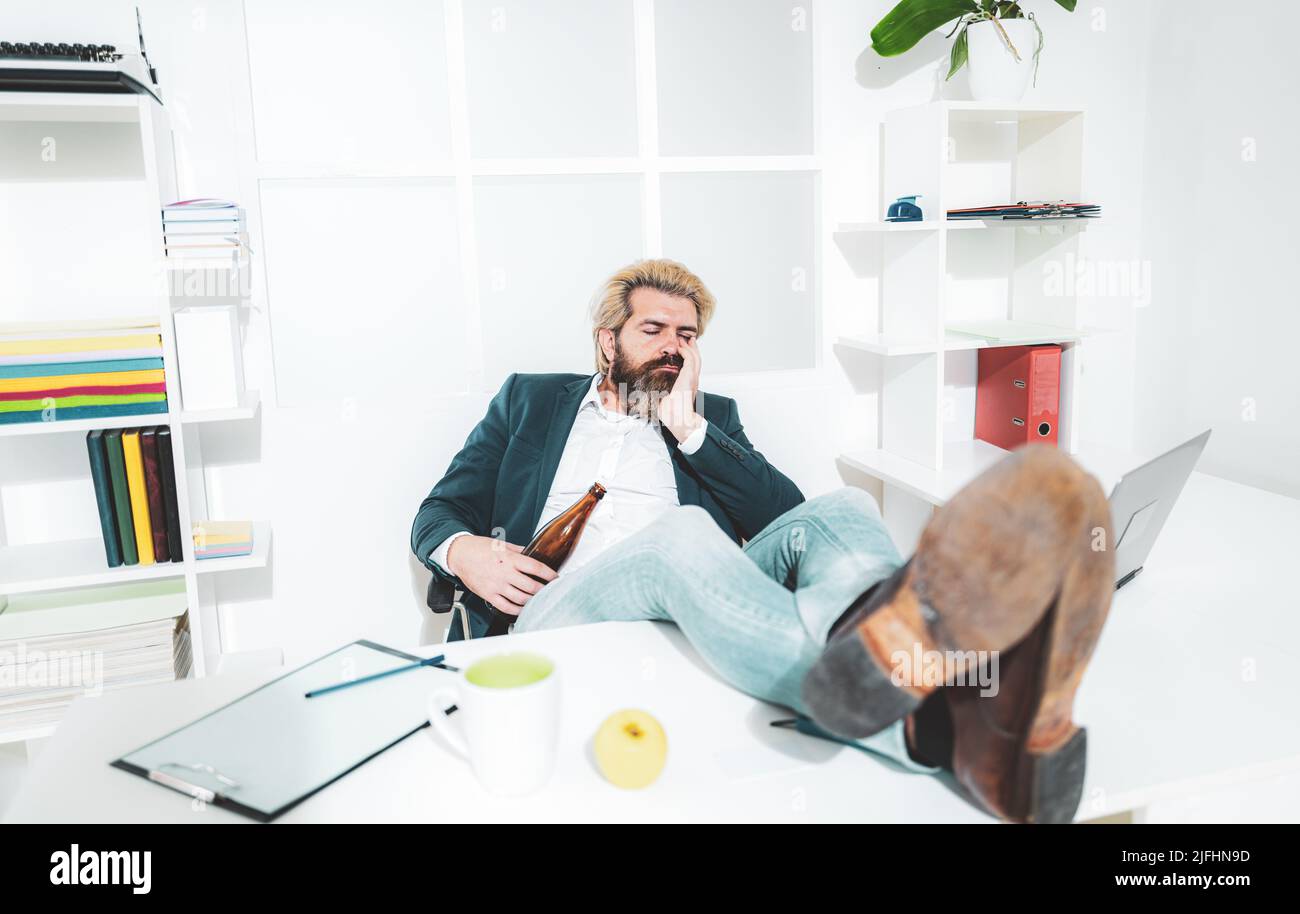 Un giovane impiegato d'affari che beve in ufficio alla scrivania. Triste stressato abuso alcolico ragazzo ottenere ubriaco sentire solo disperato circa dipendenza Foto Stock