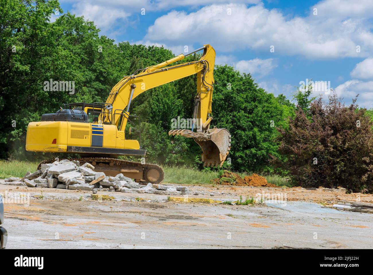 Un escavatore taglia e sgretola il vecchio frantumatore di calcestruzzo per lastre di calcestruzzo in cantiere Foto Stock