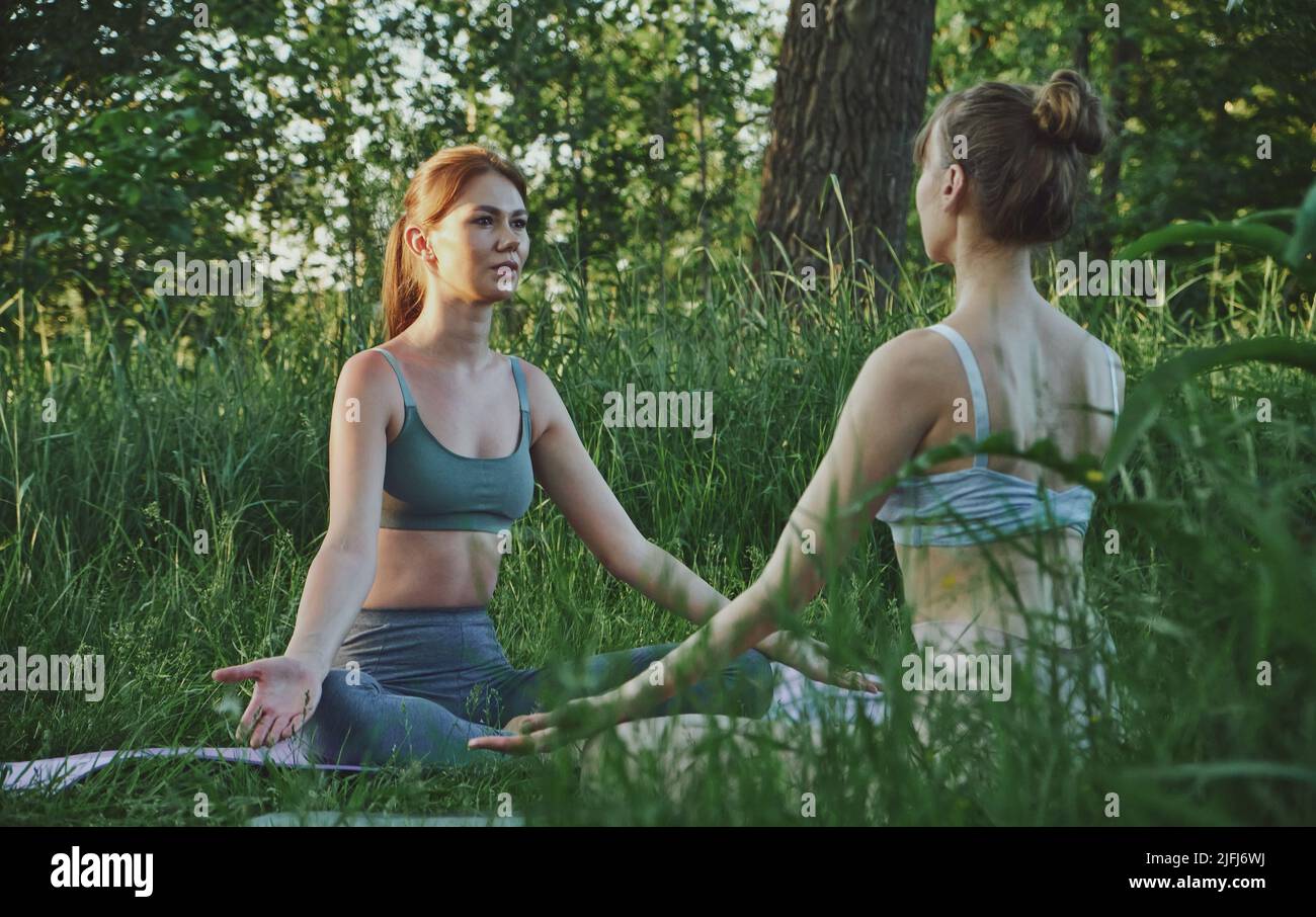 Due giovani donne che fanno yoga Padmasana Lotus posa all'aperto, meditazione e cura della salute mentale Foto Stock