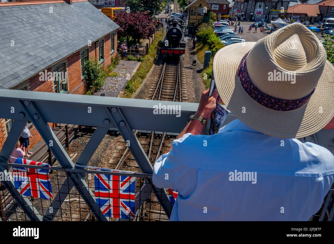 Uomo anziano che scatta una fotografia sul suo cellulare di un treno a ruscello alla stazione ferroviaria di Sheringham. Foto Stock