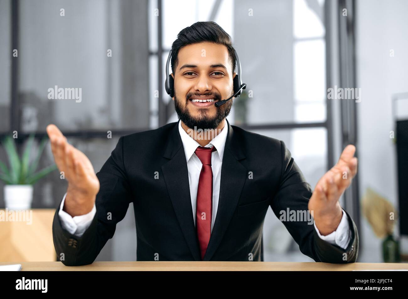 Attraente giovane uomo d'affari indiano o arabo, consulente finanziario, sedersi alla scrivania in un ufficio moderno, avendo videochiamata conversazione con il cliente, maschio economico esperto record corso di formazione online, sorriso Foto Stock