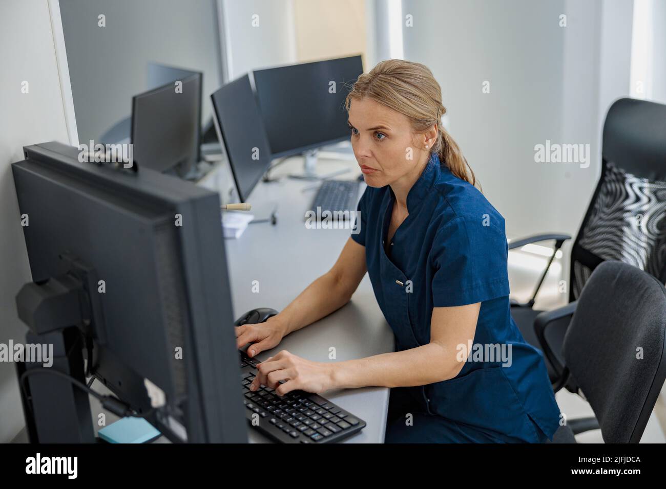 Infermiera in servizio che lavora al computer presso il banco della reception in clinica moderna Foto Stock