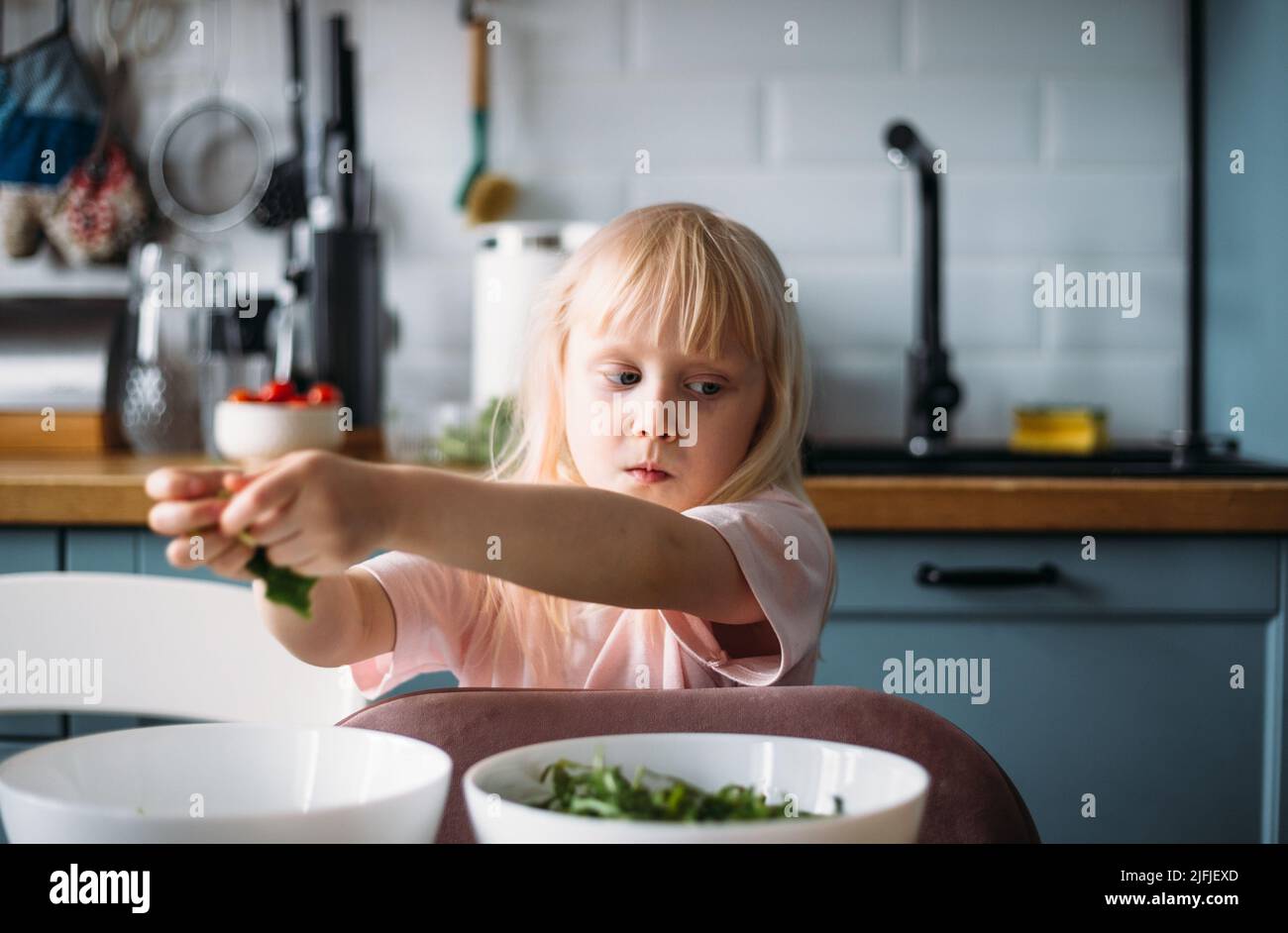 Piccola ragazza bionda sta aiutando a preparare la cena in cucina. Foto Stock