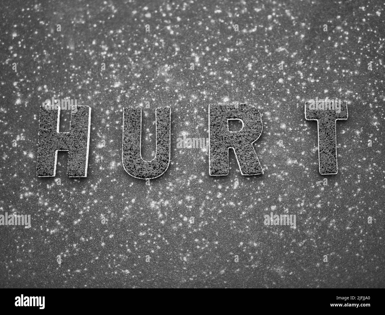 La parola 'hurt' in lettere nere su una superficie di metallo arrugginita nera. Foto Stock