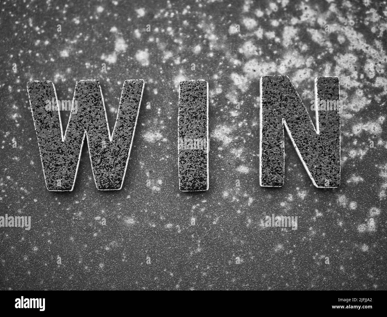 La parola 'Win' in lettere nere su una superficie di metallo arrugginita nera. Foto Stock