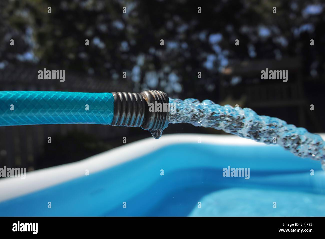 Vista ravvicinata dell'ugello nudo di un tubo da giardino, dal quale l'acqua fluisce in una piscina gonfiabile. Foto Stock