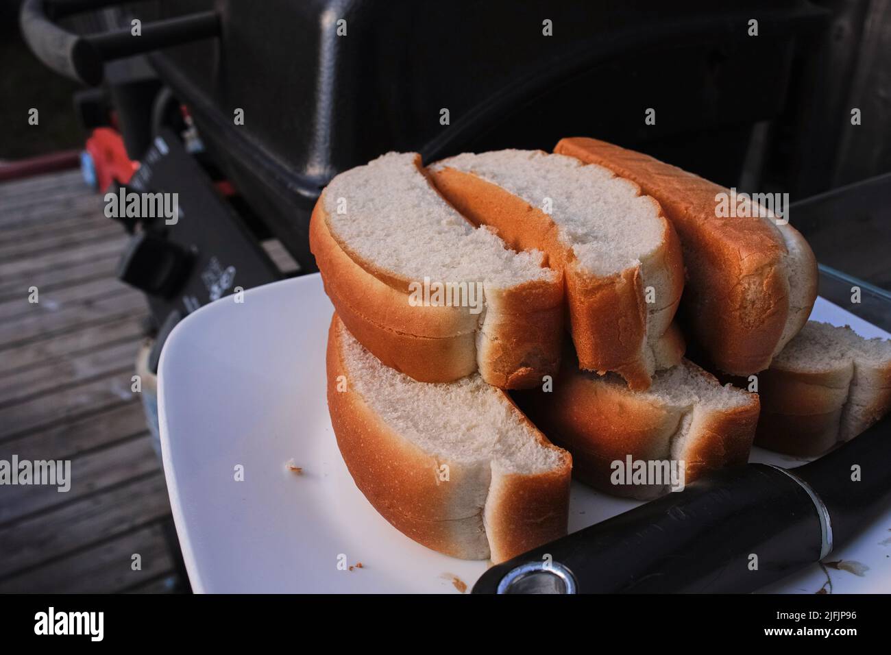 I panini con hot dog tagliati in cima si trovano accatastati su un piatto accanto a un barbecue all'aperto su un ponte. Foto Stock