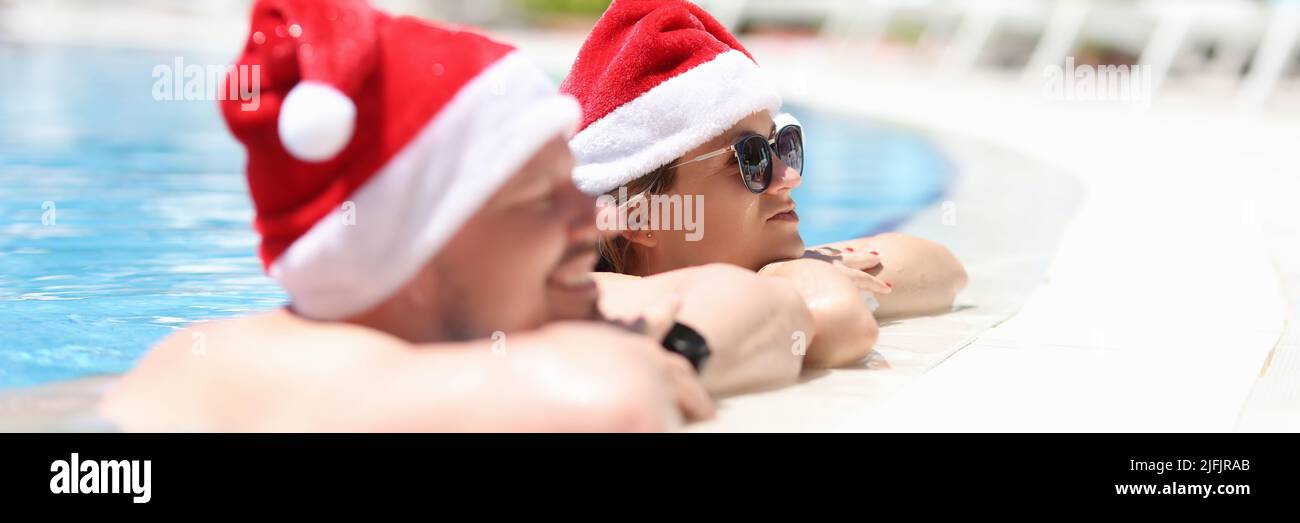 Un uomo e una donna in cappelli santaclaus stanno riposando in piscina Foto Stock