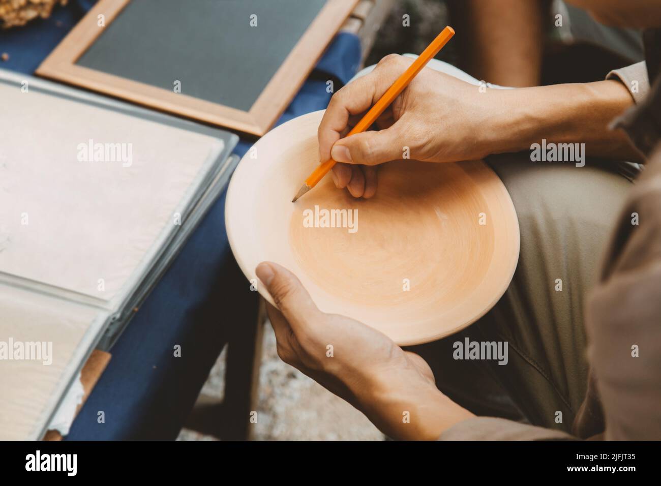 Artista disegno di disegno di disegno di Sukhothai modello di stile tradizionale su terracotta piatto, facendo di ceramica artigianale a Sukhothai, Thailandia. Foto Stock