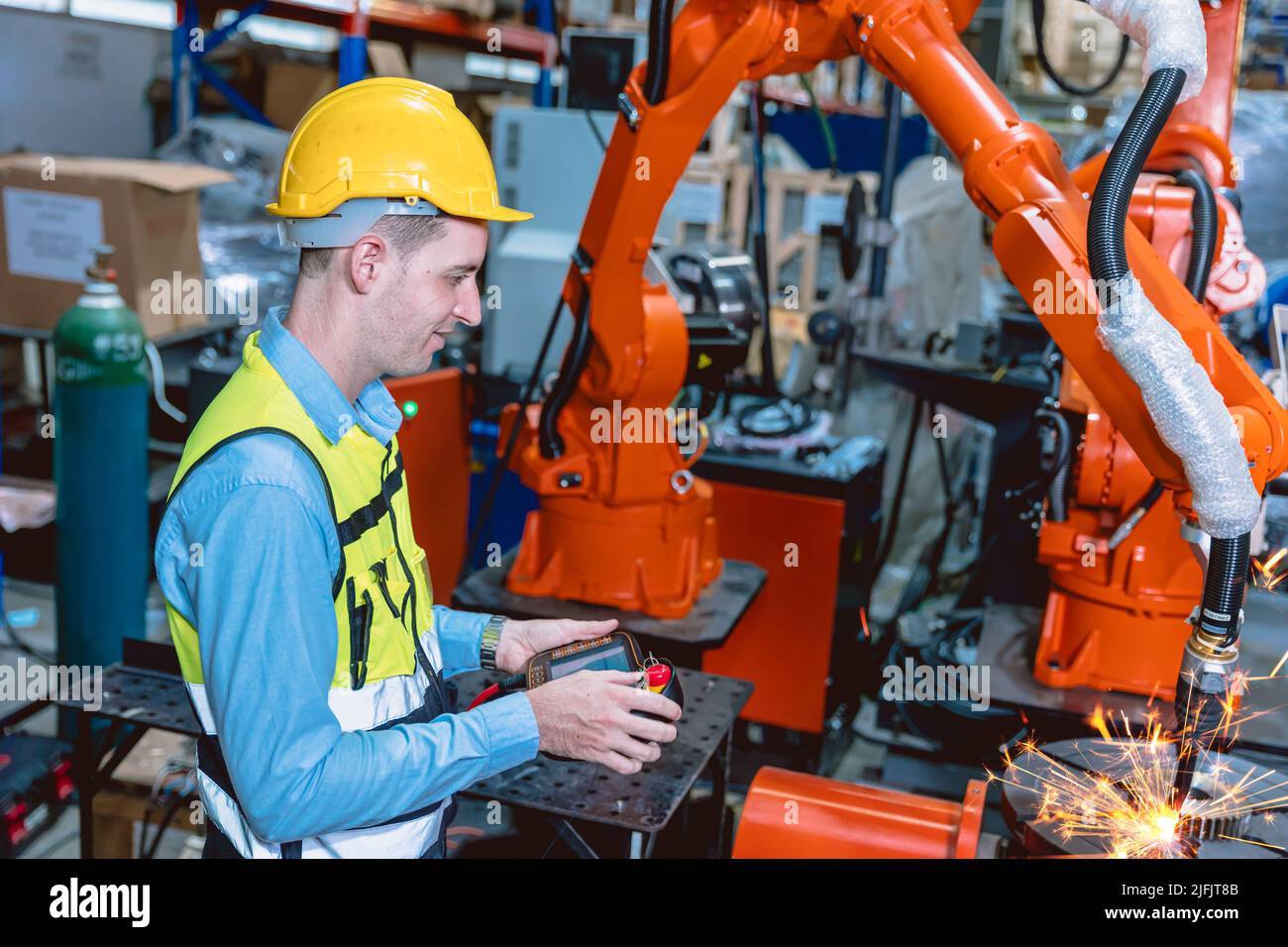 Il lavoratore che lavora con il braccio del robot automatizza la saldatrice nella moderna fabbrica di metallo. Programma di progettazione robotica nell'industria pesante. Foto Stock