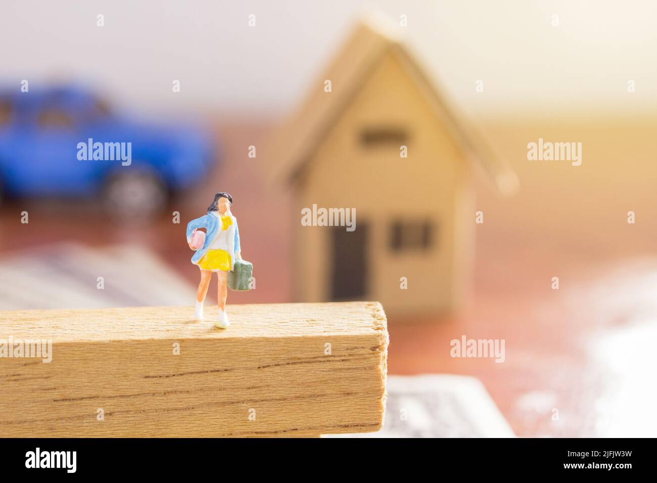 Persone in miniatura - Businesswoman borsa da trasporto in piedi sul pavimento di legno con auto blu sfocato e sfondo casa di carta. Concetto di viaggio e affari. Foto Stock