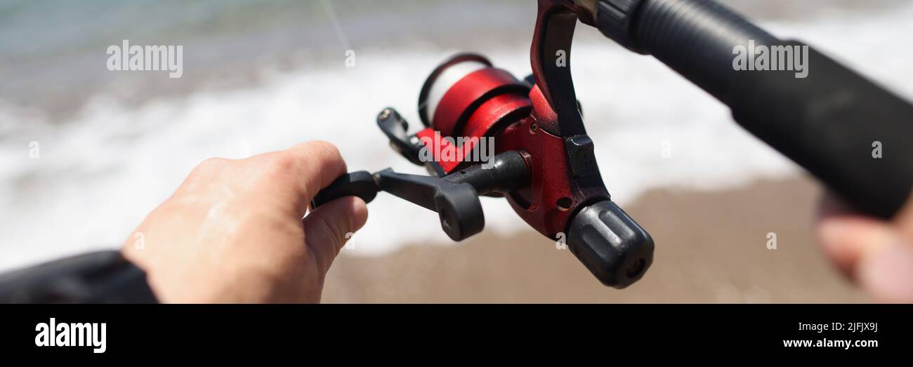 Le mani tengono una canna da pesca sullo sfondo della costa marina Foto Stock