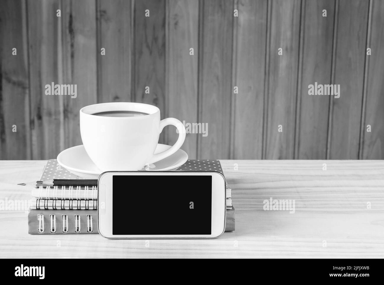 Nota libro, smartphone, tazza da caffè e pila di libri su sfondo di tavolo in legno. Tonalità bianco e nero Foto Stock